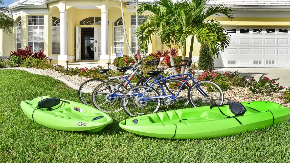 Villa Rosegarden - A yellow house with a tropical garden, two green kayaks, and two bicycles in the foreground.
