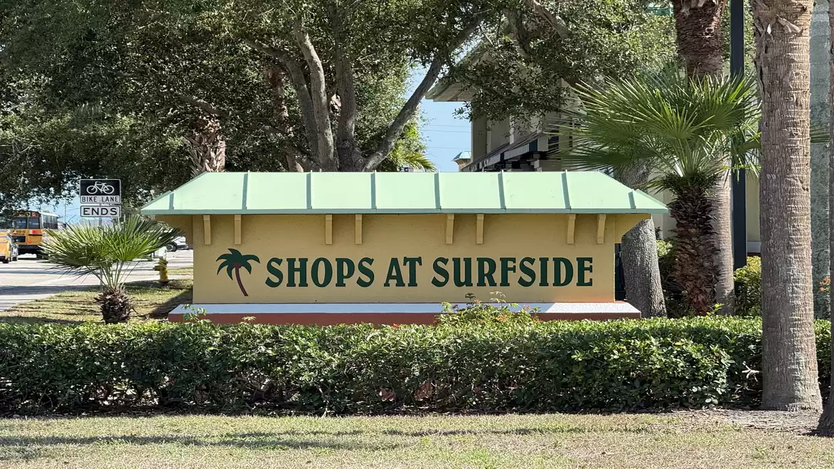 A sign reading 'Shops at Surfside' is set in a landscape with trees and grass.
