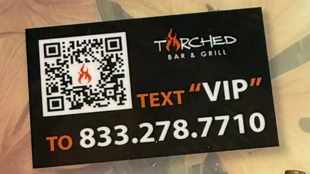 Advertisement for Torched Bar & Grill featuring a QR code with a flame symbol, next to the text 'Text VIP to 833.278.7710'.