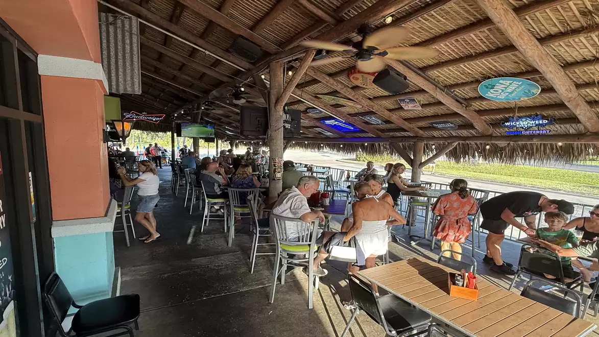 A busy outdoor restaurant with a wooden roof, patrons at tables, and people enjoying the relaxed atmosphere.