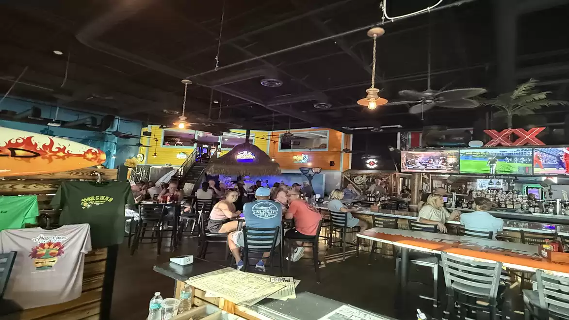 A busy restaurant with a bar, people at tables, and bright lights, creating a cozy and welcoming atmosphere.