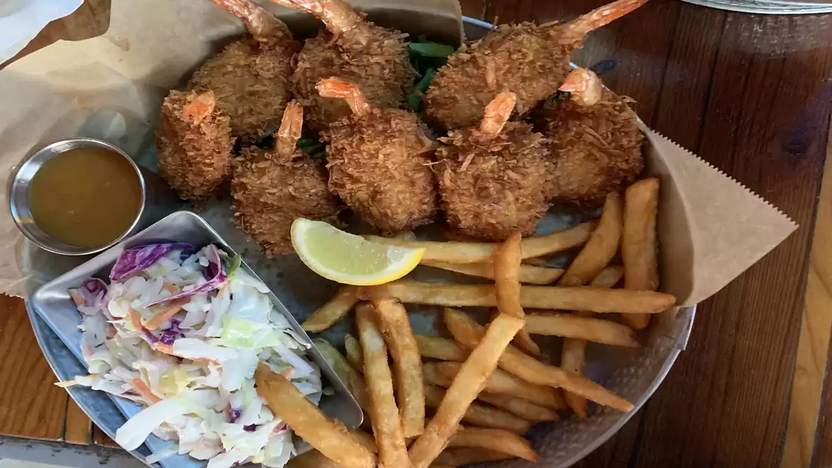 A plate with crispy fried shrimp, French fries, coleslaw, and a lemon slice, served with a sauce.