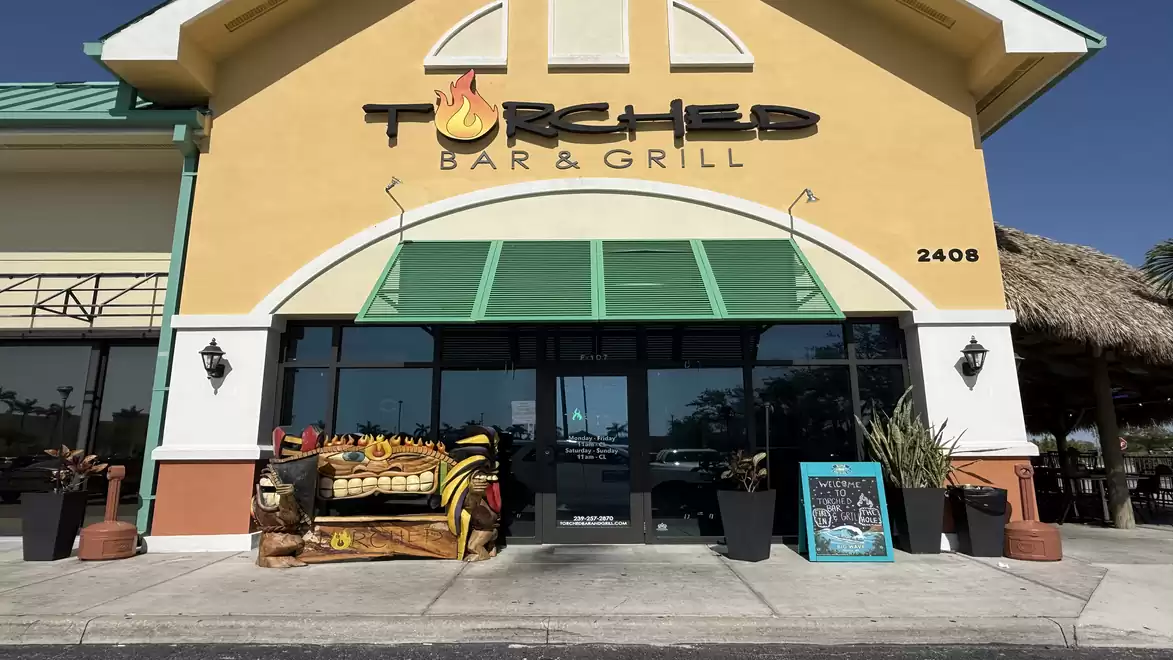 Exterior view of a yellow restaurant called Torched Bar & Grill with a green roof and decorative plants.