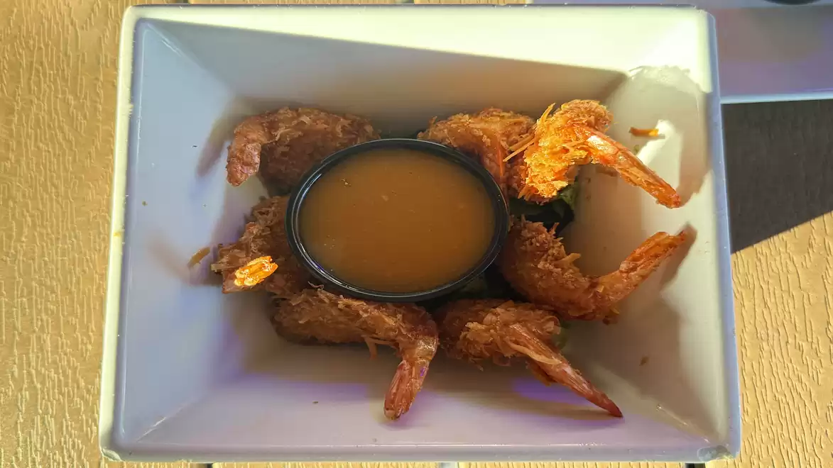A square white dish containing several fried shrimp arranged in a circle around a bowl of sauce, on a wood-colored table.