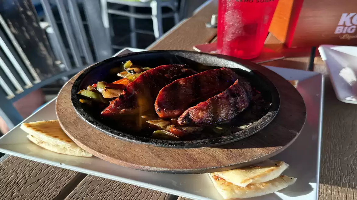 A plate with grilled food including sausage, vegetables, and bread, served on a table.