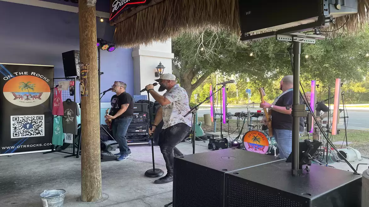 Live band performing music on an outdoor stage with microphones and guitars, surrounded by exotic decor.