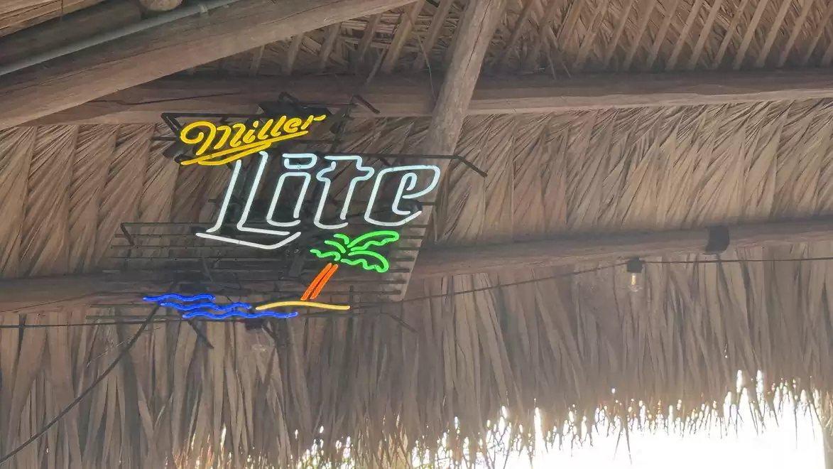 Neon sign for Miller Lite in a thatched roof building with a ceiling view.