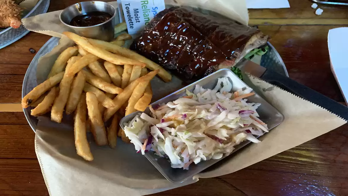 A plate with French fries, coleslaw, and ribs, served with barbecue sauce.
