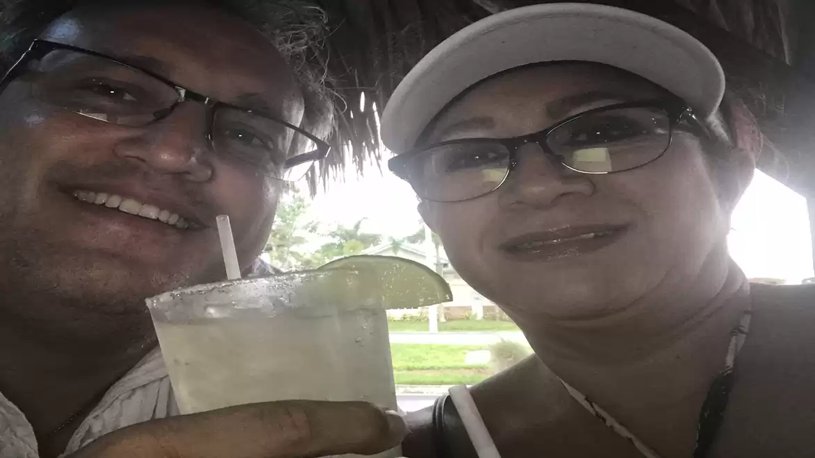 Smiling couple with glasses enjoying a lime cocktail on vacation under a thatched roof.
