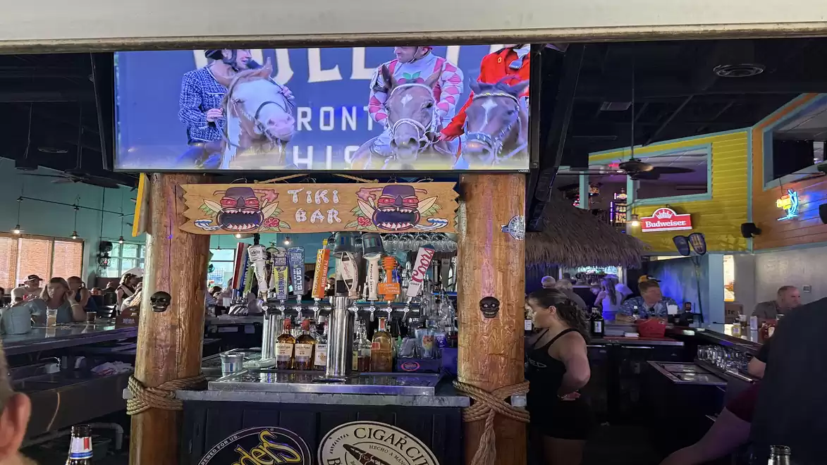 A tiki bar with wooden decoration and taps in a busy, well-attended bar with televisions and neon lights.