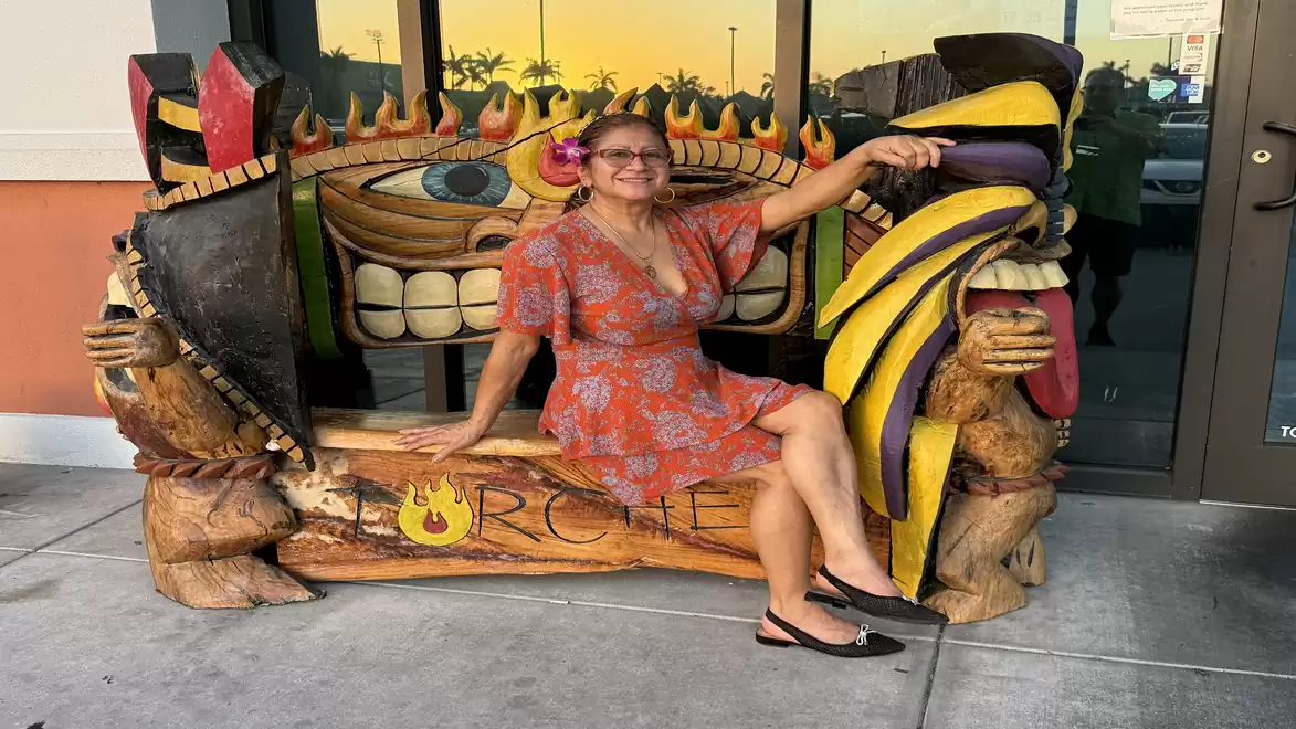 Woman in a red dress sitting on a colorful, sculptural wooden bench with carved faces.