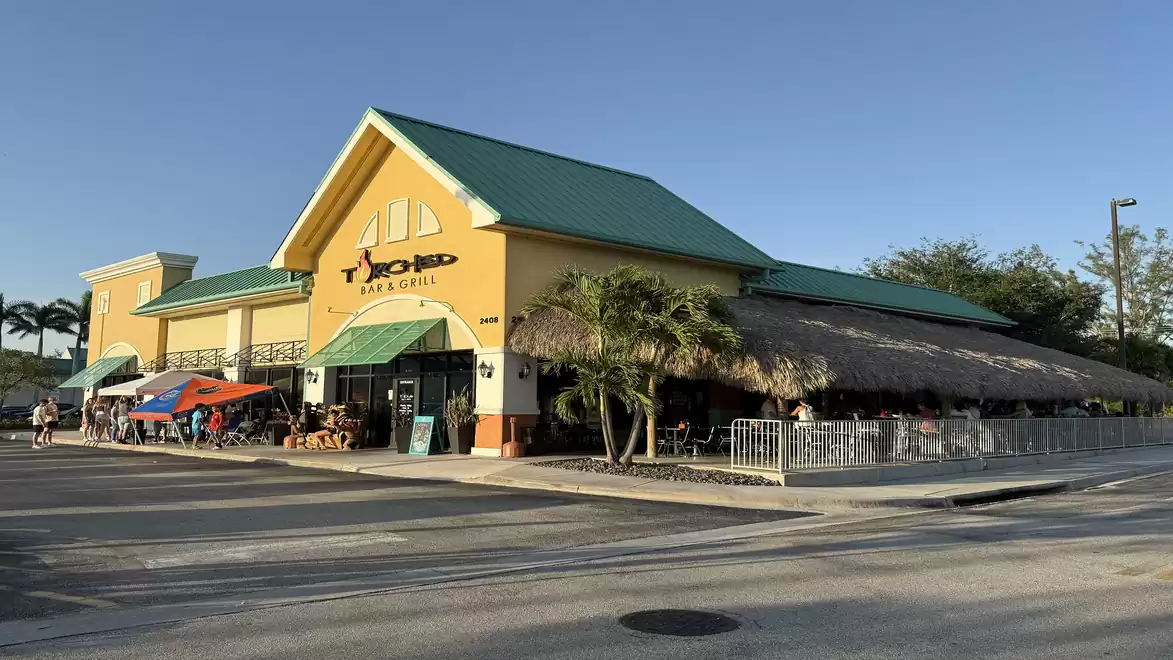 Yellow restaurant building with green roofs and palm trees in the foreground under clear sky.