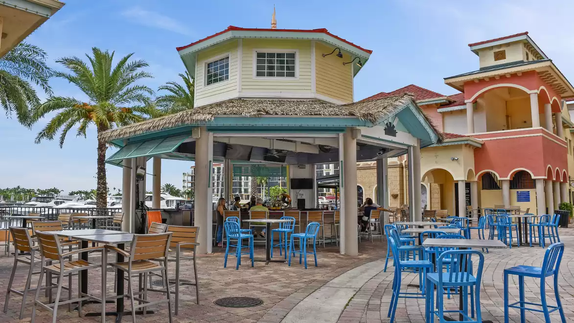 A cozy outdoor area with blue chairs and a pavilion in a tropical setting, palm trees in the background and a clear sky.