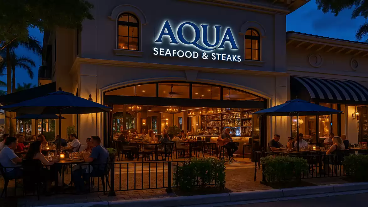 Exterior view of a restaurant named Aqua Seafood & Steaks at night, with guests sitting at tables outside.