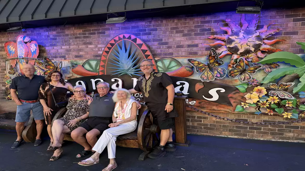 A group of people joyfully posing in front of a colorful wall with tropical motifs and the text 'Senoritas'.