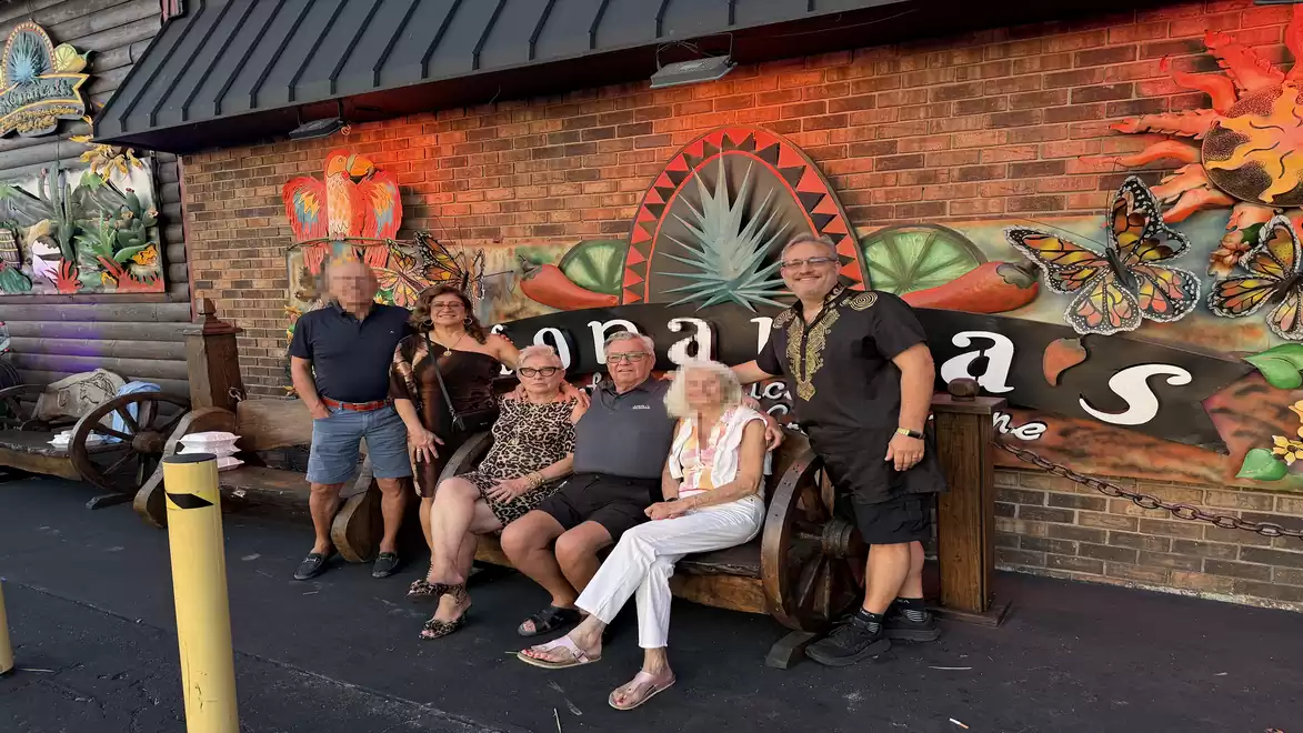 Group of people sitting on a bench in front of a colorful wall with tropical design.