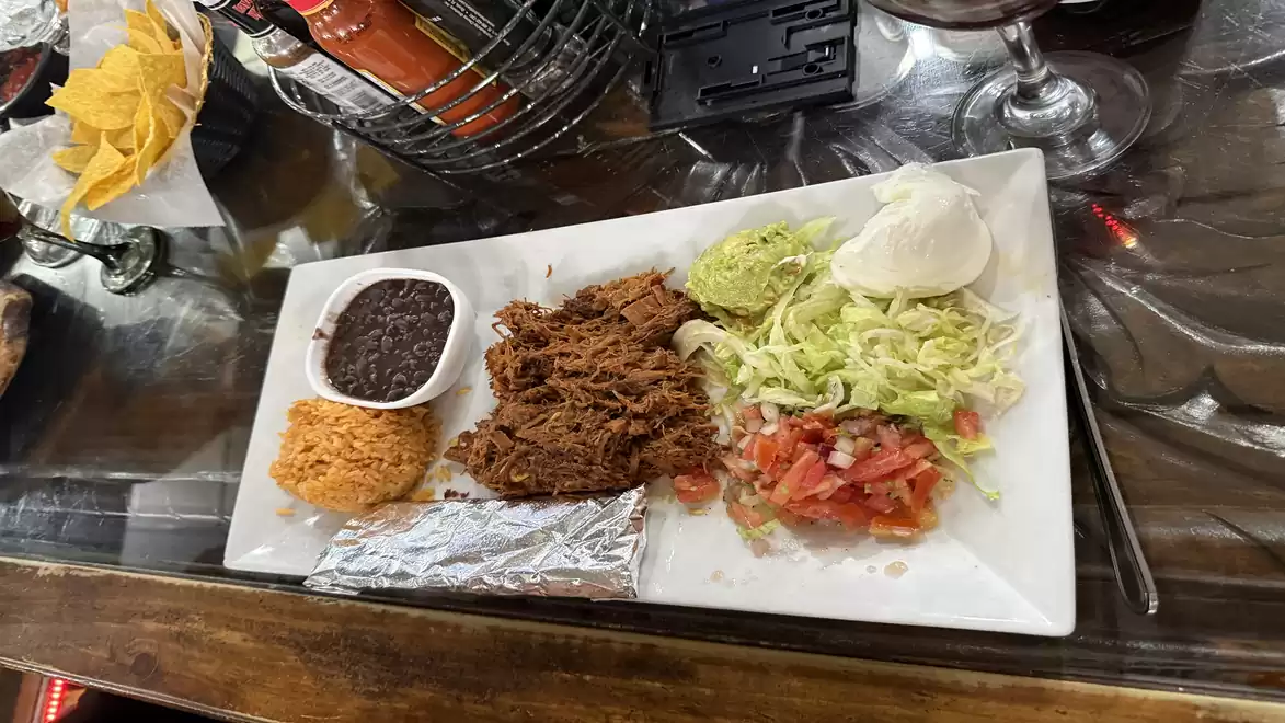 A plate with Mexican dishes, including beef, rice, beans, lettuce, sour cream, tomatoes, and a tortilla.