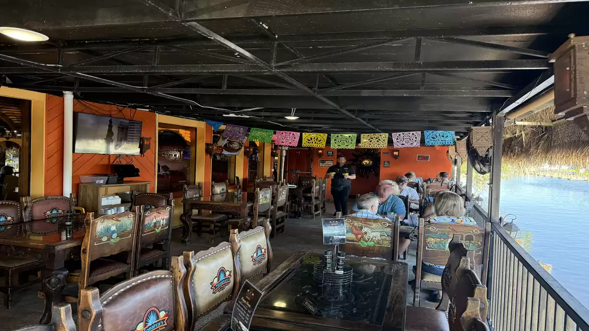 Interior view of a lively Mexican restaurant with colorful decorations and wooden furniture, offering a view of the water on a sunny day.