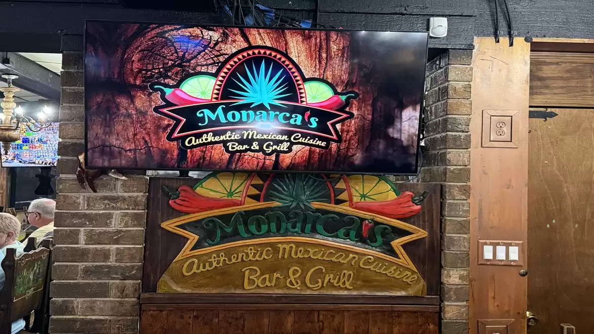 Interior view of a Mexican restaurant featuring two signs for Monarca's Authentic Mexican Cuisine Bar & Grill, one on a screen and one hand-painted on wood.