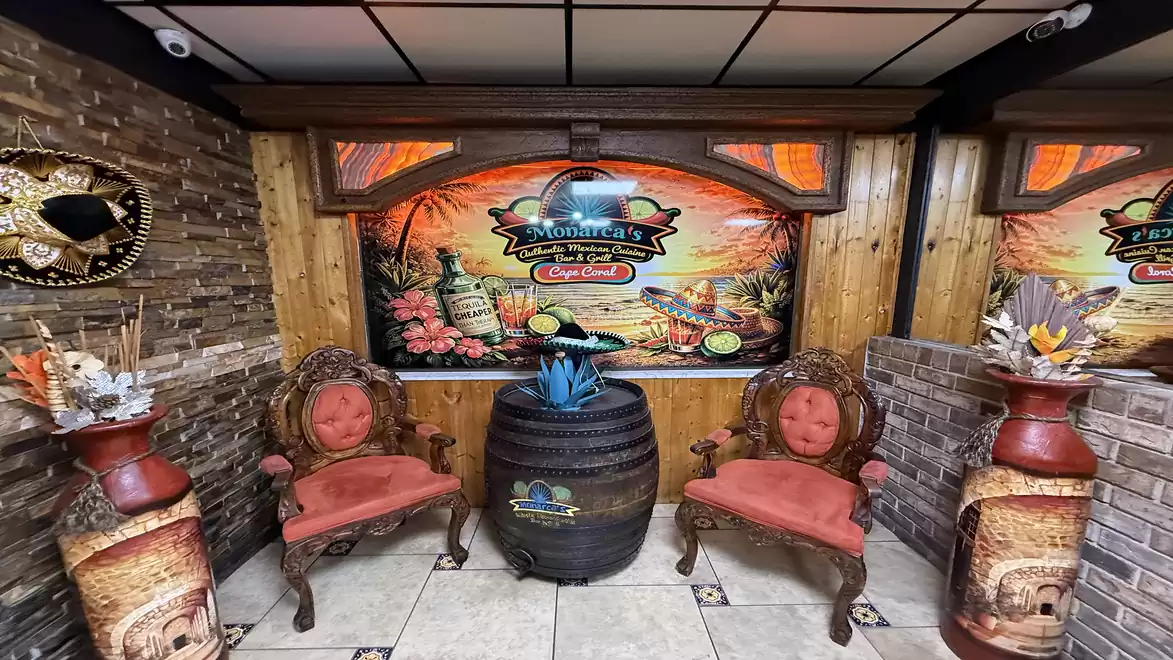 A rustic room with two decorative armchairs, a wooden barrel as a table in the center, surrounded by Mexican decorations and a colorful mural.