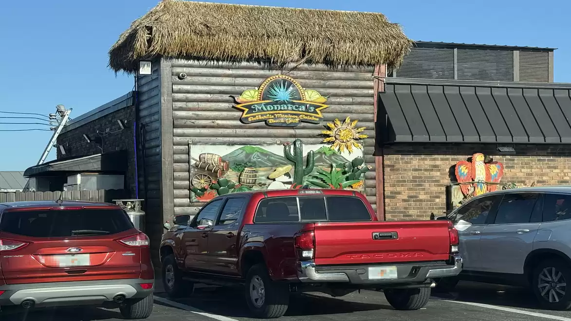 Red and white cars parked in front of a restaurant with thatched roof and mural on a sunny street.