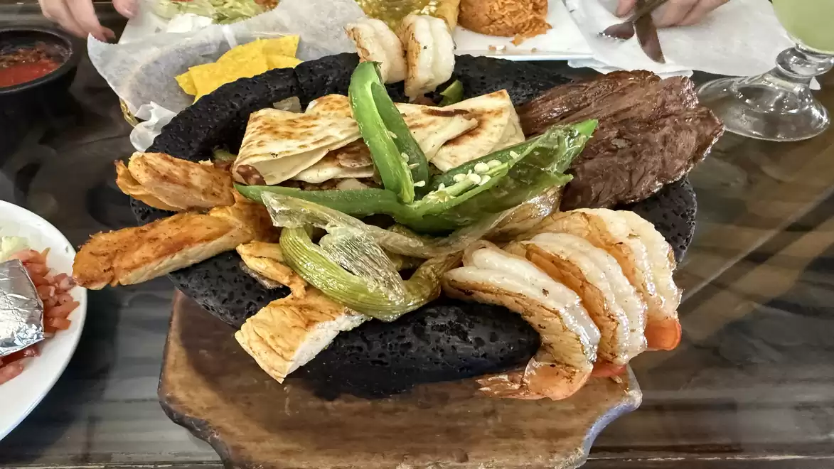 A traditional Mexican dish served on a table, consisting of grilled meat, shrimp, peppers, and flatbread.