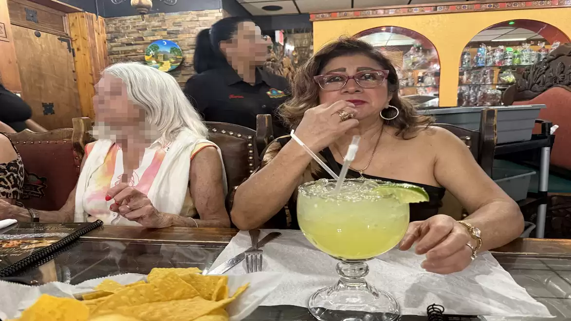 Woman in a restaurant enjoying a large glass of margarita next to an older woman with chips on the table.