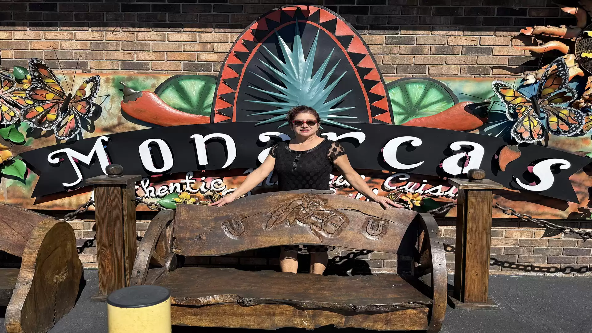 A woman sits on a wooden bench in front of a colorful sign reading 'Monarca's Authentic Mexican Cuisine'.