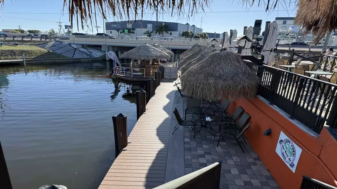 A wooden dock runs along the water with thatched roofs and a modern building in the background.
