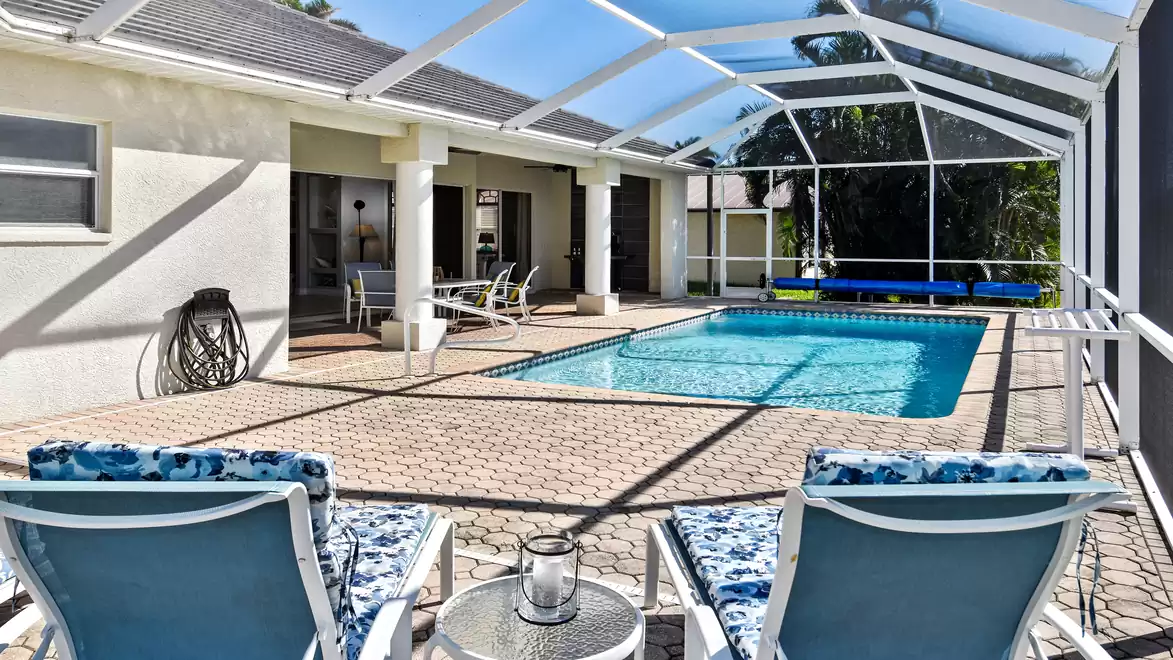 Villa Boaters Dream - A modern pool area with blue loungers, a table, and a glass-covered roof in a sunny courtyard.