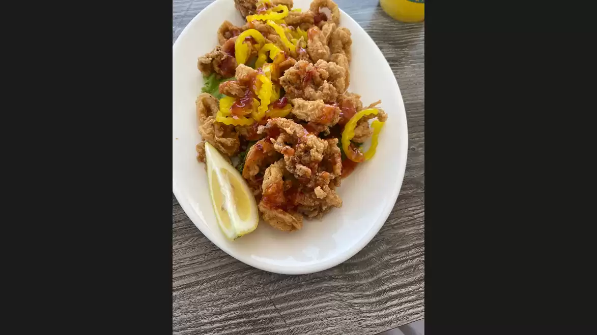 A plate of crispy calamari, garnished with sliced peppers and a lemon wedge on a wooden table.