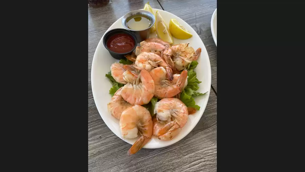 Shrimp platter with lemon wedges and dipping sauces on a white plate.