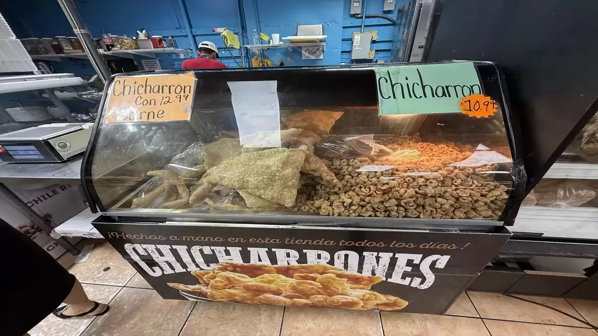 A food display in a store labeled 'Chicharrones', filled with fried snacks and price tags.
