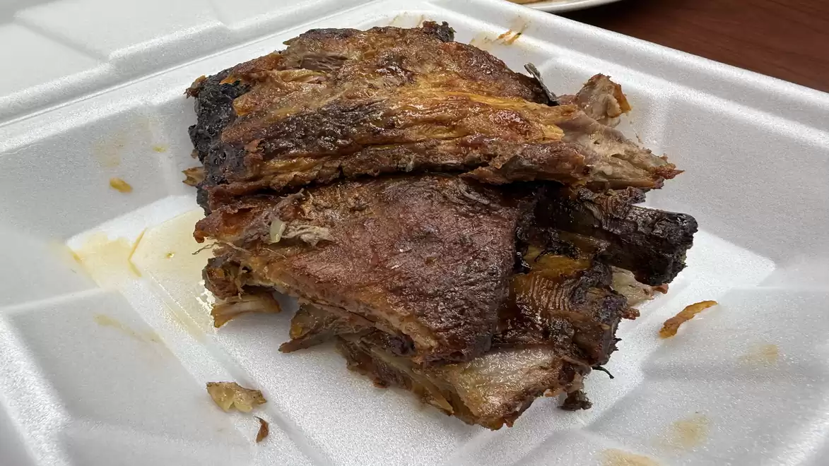 A stack of juicy grilled ribs in a white foam container.