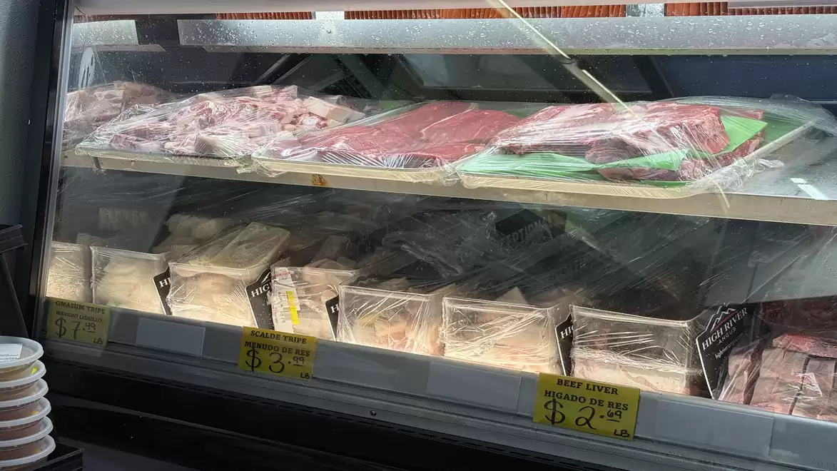 Meat counter with various packaged meat products wrapped in plastic film, with price tags.