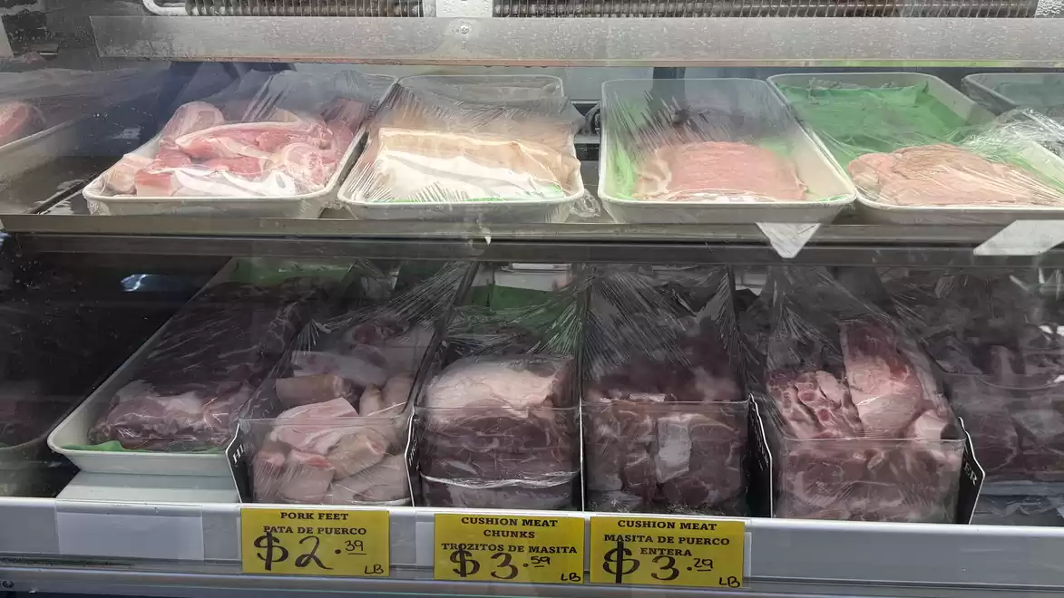 Meat counter displaying various types of meats in plastic packaging, priced with yellow tags.