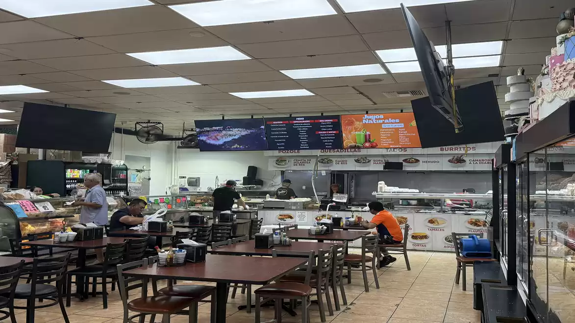Interior of a modern fast-food restaurant with empty tables, a food counter, and digital menu boards on the wall.