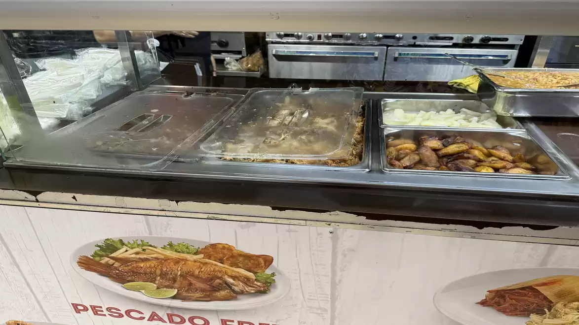 A buffet counter in a restaurant with hot food containers, including fish and fried bananas, on a white table with images of dishes.