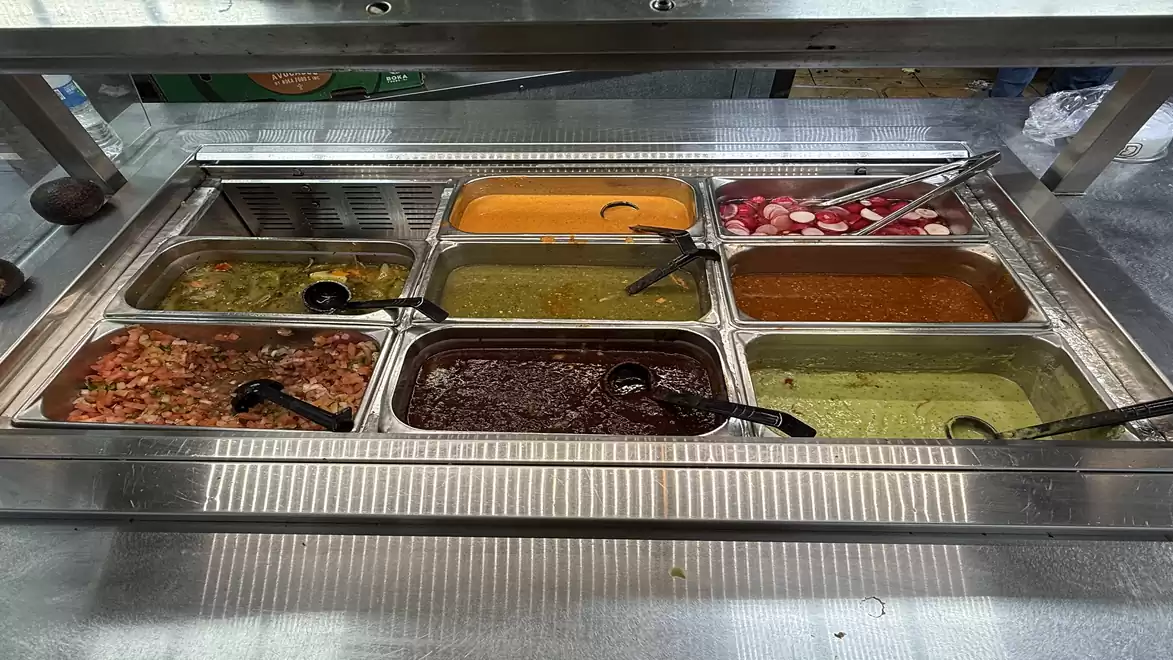 Self-service counter with various sauces and dips, including salsa, guacamole, and black beans.