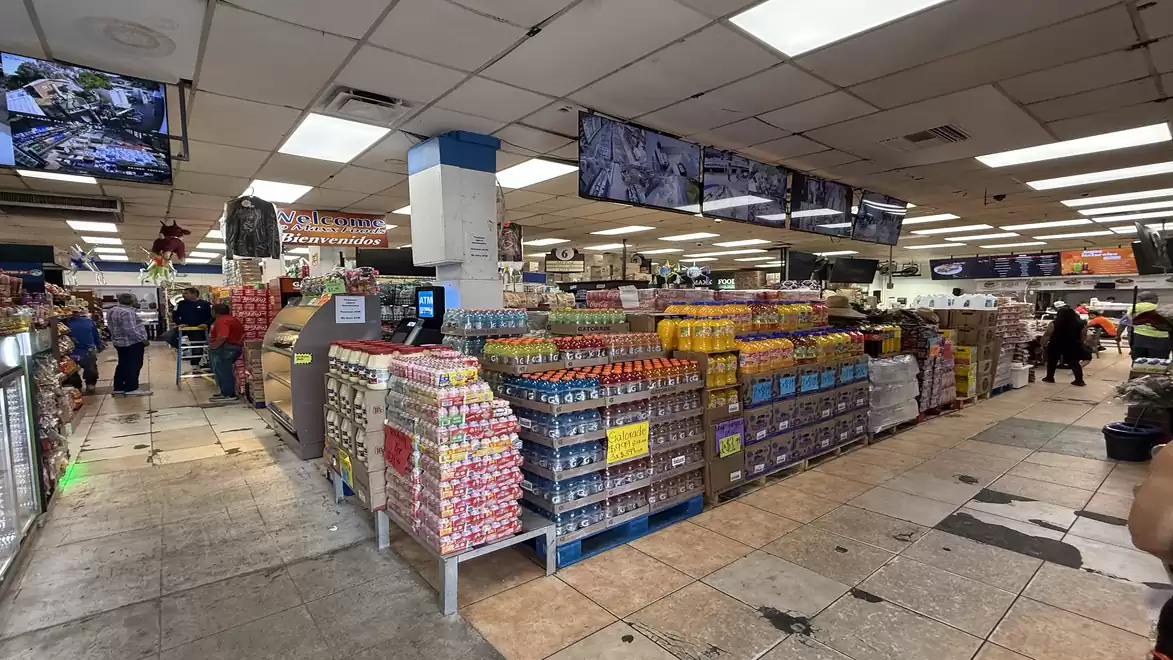 A supermarket with shelves full of various products, including drinks and groceries, and several screens on the ceiling.