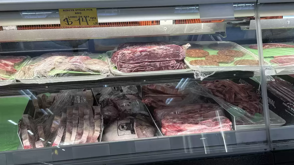 A supermarket meat counter with a selection of packaged meat cuts, including steaks, minced meat, and smoked bacon.