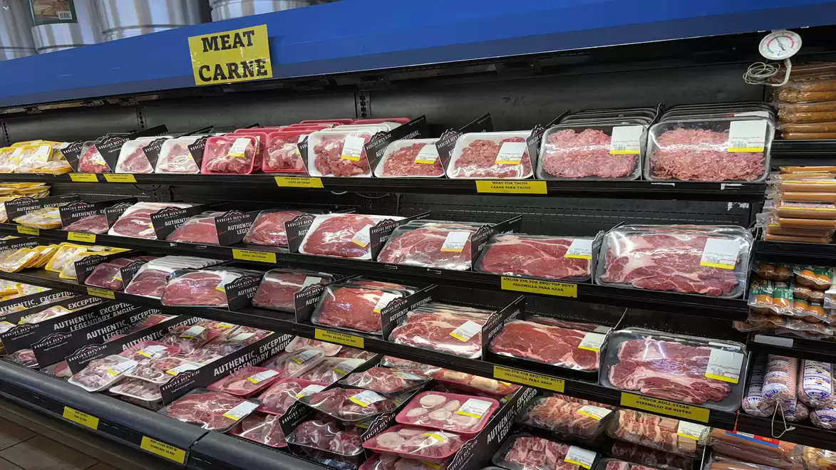 Supermarket shelf with various types of meat in plastic packaging, yellow price tags are visible.
