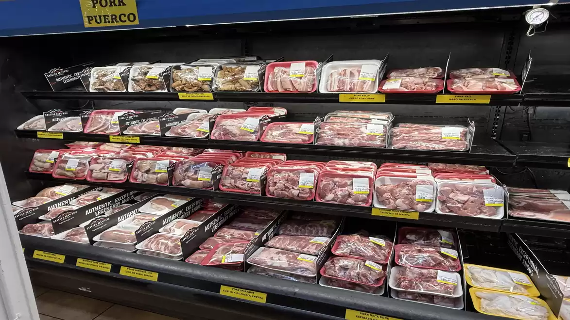 A supermarket shelf with various packages of pork stacked in multiple rows.
