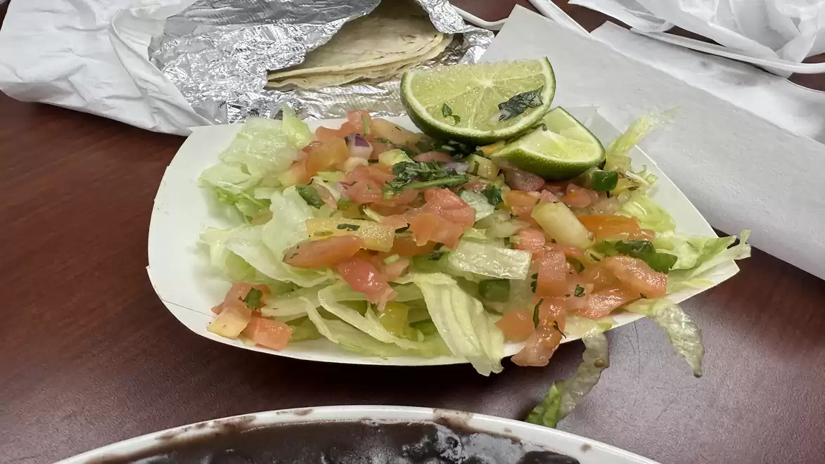 A close-up of a taco salad on a table with lime slices and wrapped tortillas in the background.