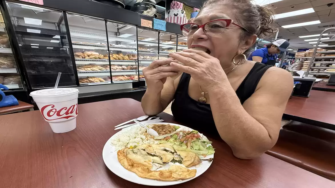 A woman with glasses eating a meal with vegetables and meat in a café, with a cup of Coca-Cola beside her.