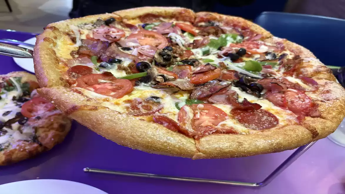 Close-up of a freshly made pizza with various toppings such as salami, pepperoni, olives, and mushrooms on a table.