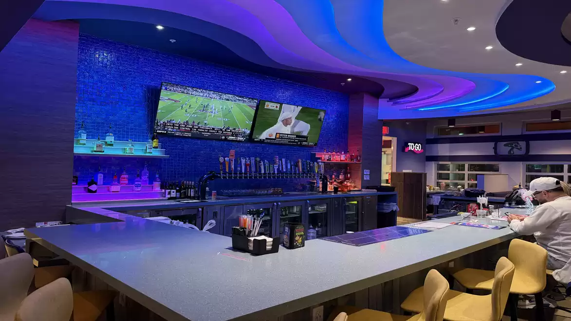 Modern bar with illuminated ceiling and TVs showing sports.