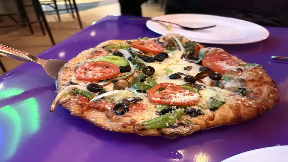 Vegetarian pizza with tomatoes, olives, and spinach on purple table