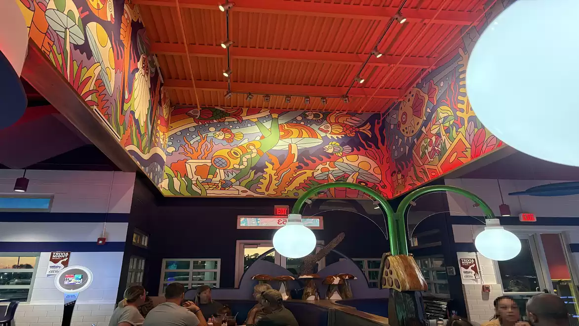 Vibrant restaurant with colorful murals and modern lamps; people are sitting relaxed at tables.