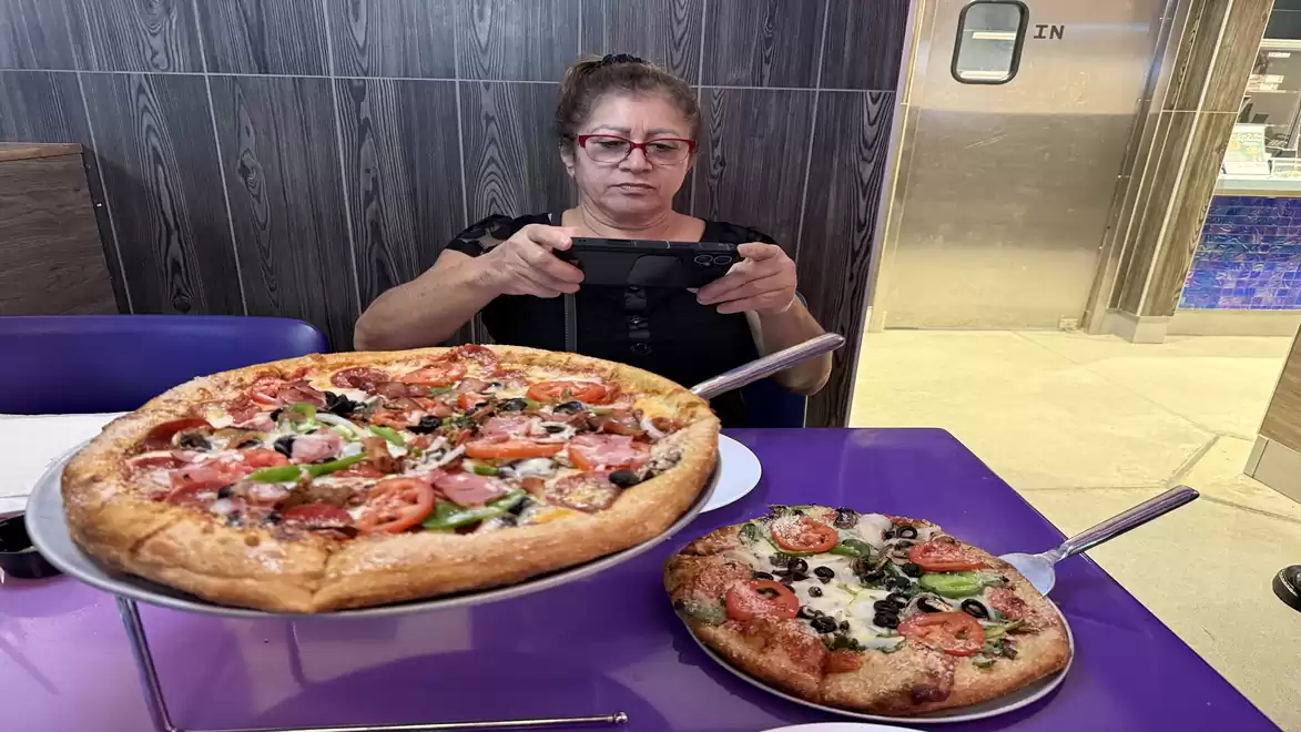 Woman photographing two pizzas on a table in a restaurant.